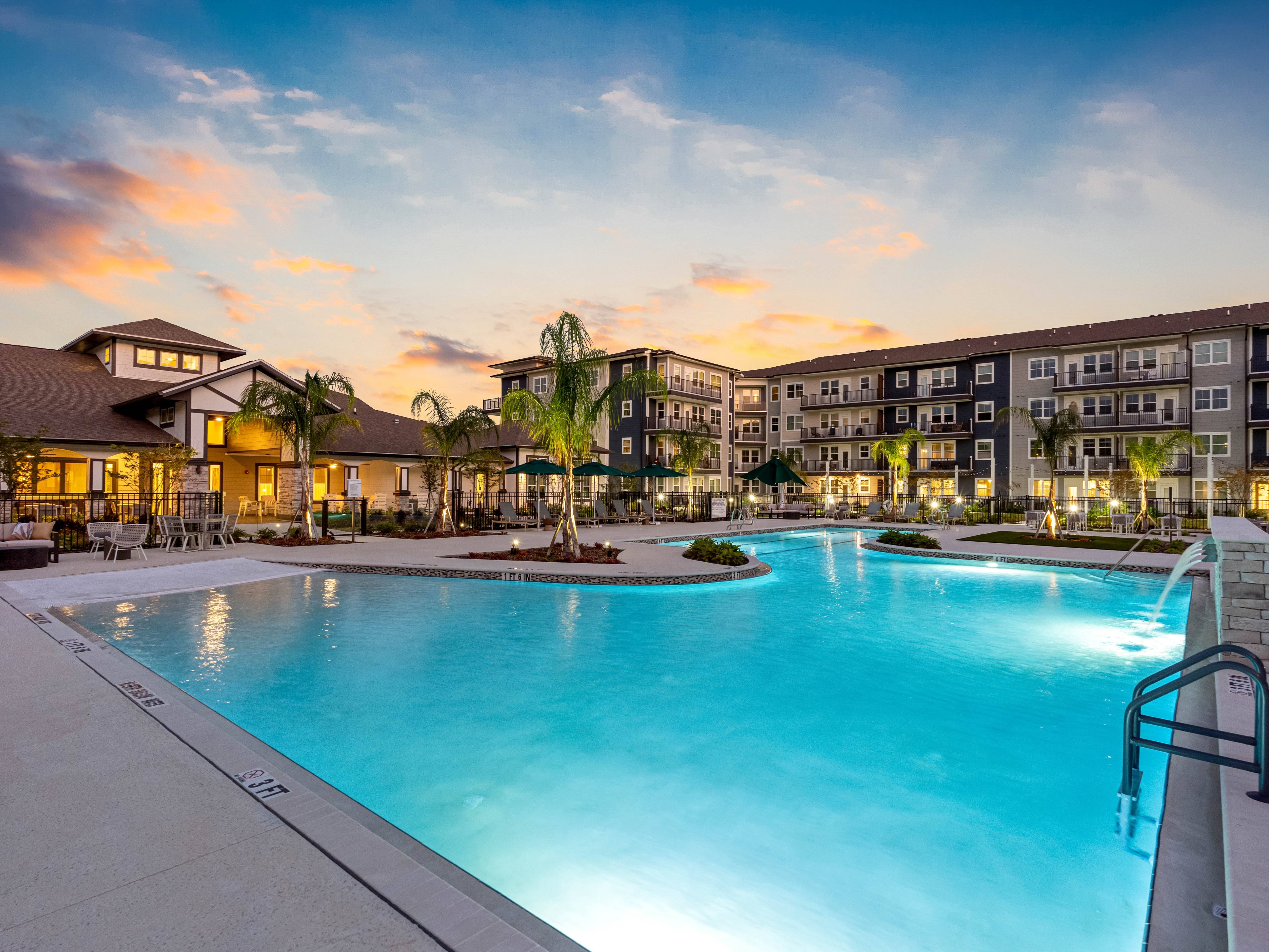 A large swimming pool in front of apartment buildings at dusk.